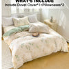 A bed set featuring an elegant floral tea art duvet cover, two pillowcases, and a green accent pillow on a light-colored bed.