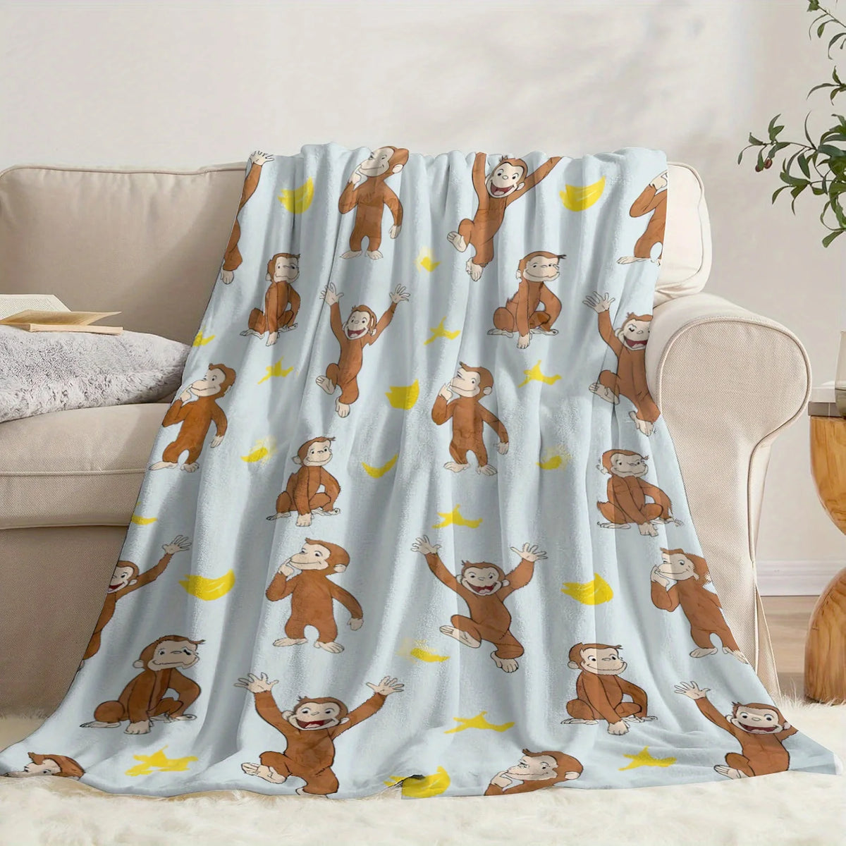 A light blue flannel throw blanket featuring repeating illustrations of Curious George characters.
