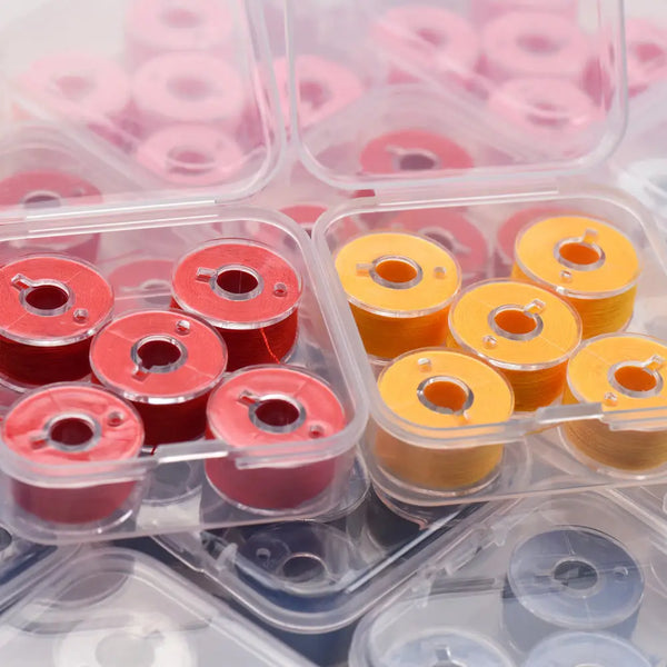 A collection of prewound sewing machine bobbin threads in various colors, including pink, red, and yellow, packaged in clear 