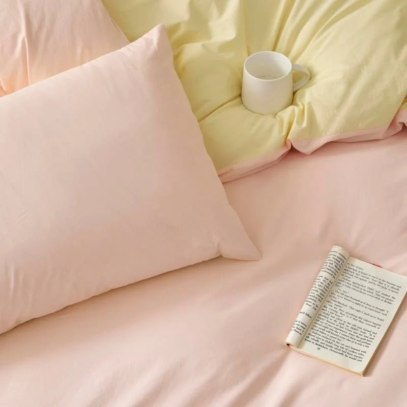 A pink duvet cover set with matching pillowcases and a white mug on a light yellow bed.