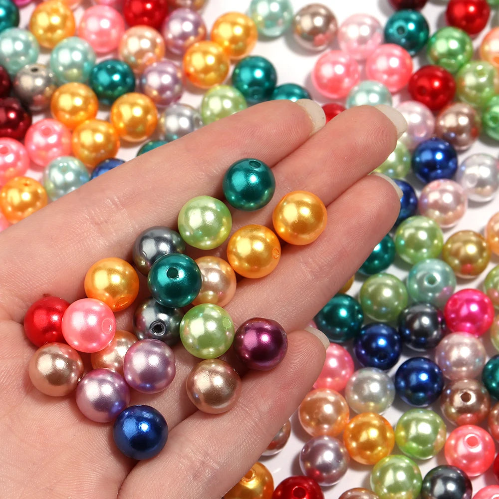 A hand holds a variety of colorful imitation pearl beads for DIY jewelry making.
