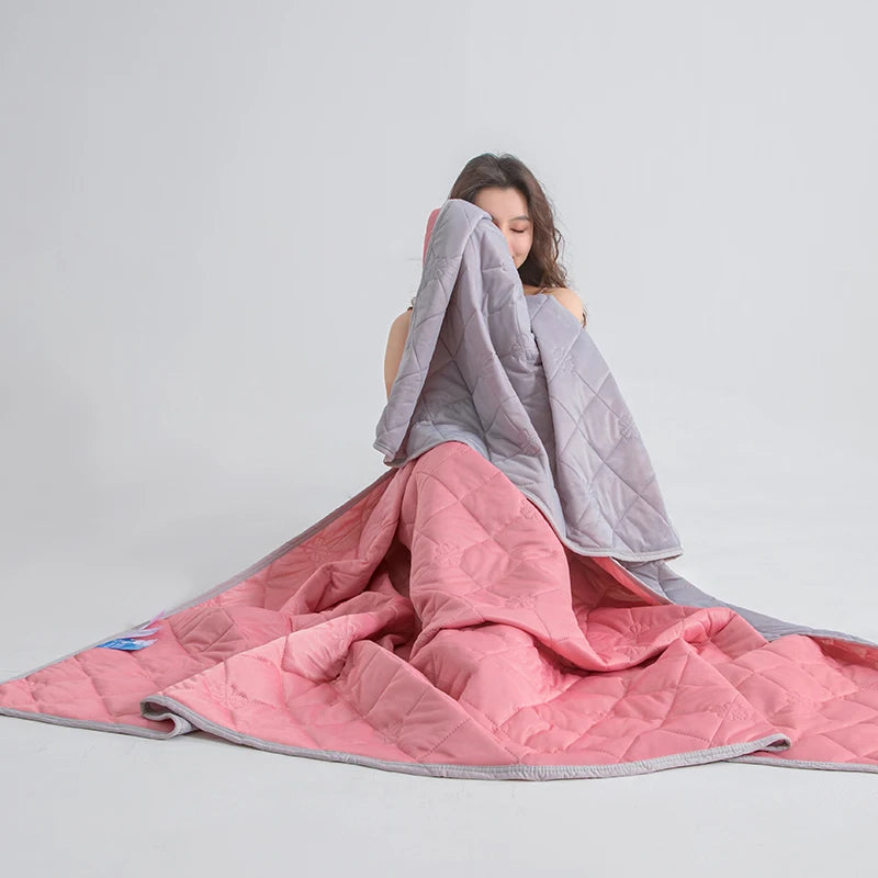A person is draping a pink quilted blanket over their head, with the blanket spread out on a light gray background.