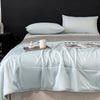 A light blue lightweight cooling blanket is displayed on a bed with matching pillows and a candle.