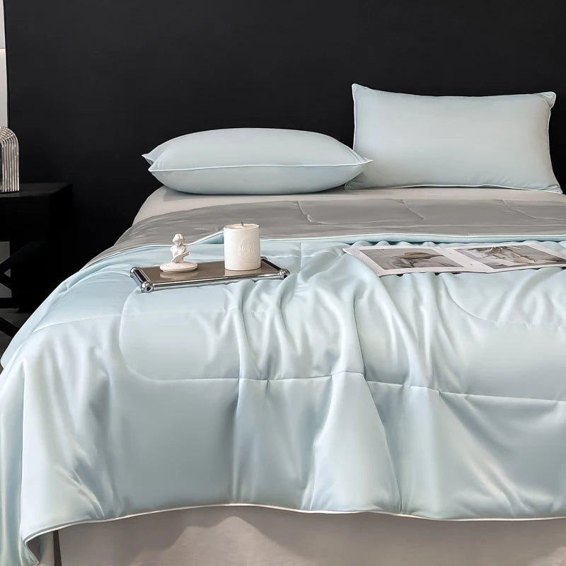 A light blue lightweight cooling blanket is displayed on a bed with matching pillows and a candle.