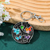 A silver enamel pin keychain featuring a colorful, abstract design on an oval background, resting on a wooden surface.