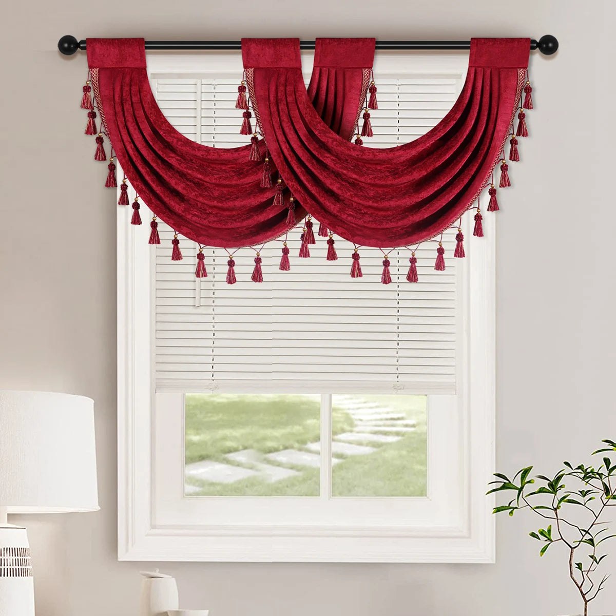 A deep red European style window curtain valance with tassels draped over a white window frame.