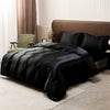 A black satin luxury bedding set is displayed on a bed with a brown headboard and light-colored curtains.