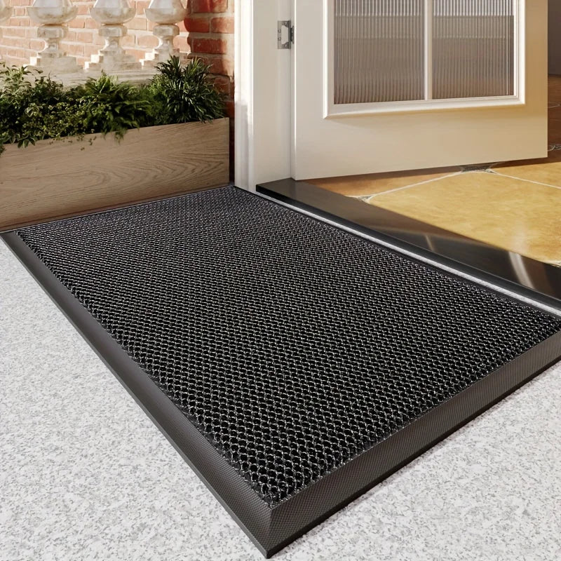 A black non-slip rubber mat is placed on a light gray floor in front of a white door frame.