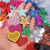 A hand holds a collection of glitter iron-on embroidered love heart and star patches in various colors.