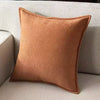 A square, rust-colored chenille throw pillow resting on a light beige sofa.