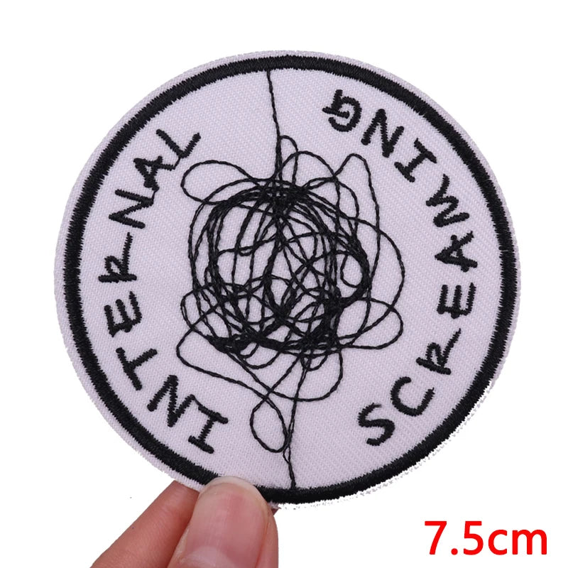 A round embroidered patch with the text INTERNALING SCREAMING stitched in black thread on a light pink fabric.