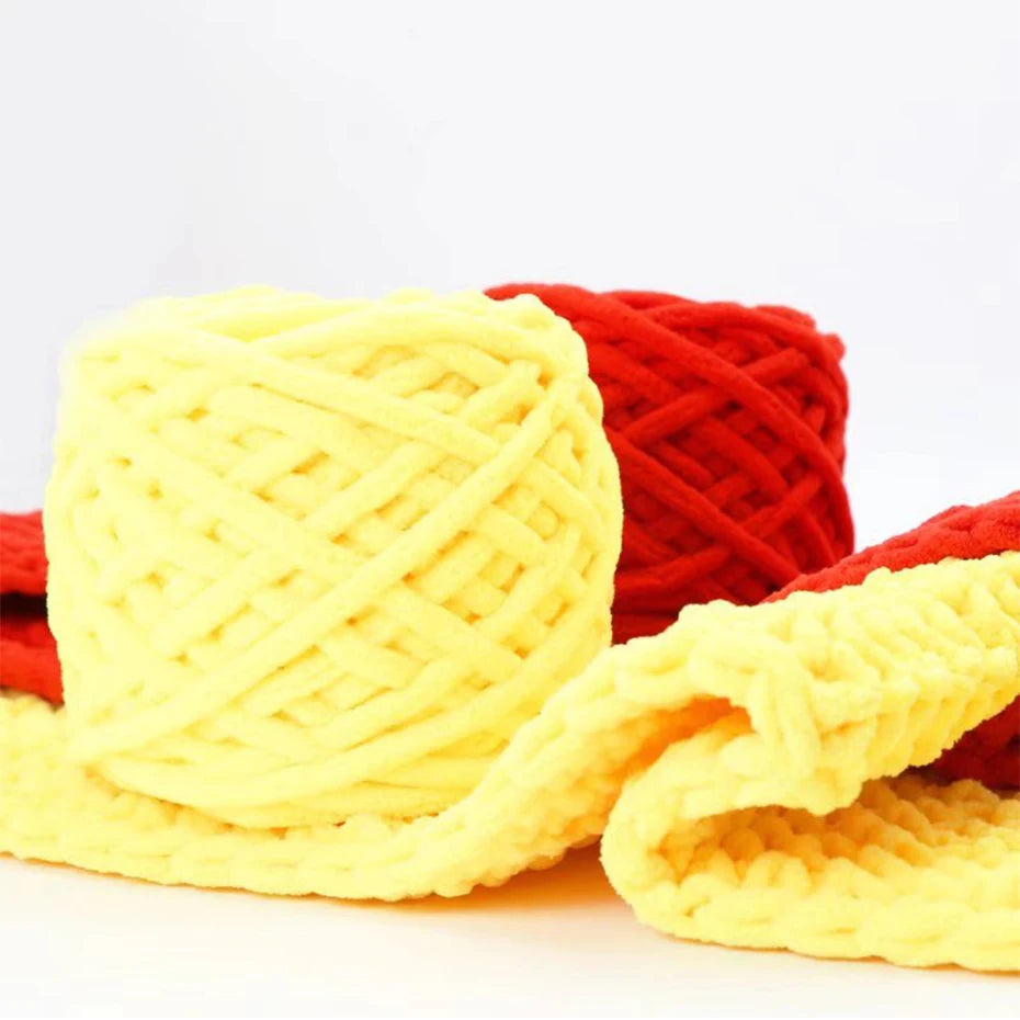 A ball of chunky yellow velvet knitting yarn next to a bundle of red yarn.