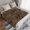 A luxurious leopard print flannel blanket is displayed on a bed with white linens and gray textured fabric.