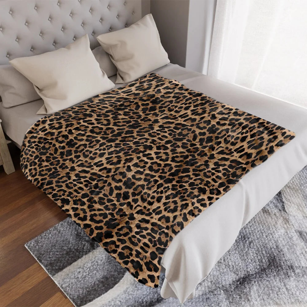 A luxurious leopard print flannel blanket is displayed on a bed with white linens and gray textured fabric.