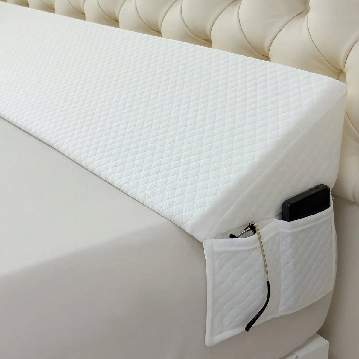 A white adjustable bed wedge pillow with a quilted cover is shown resting on a white bed surface.