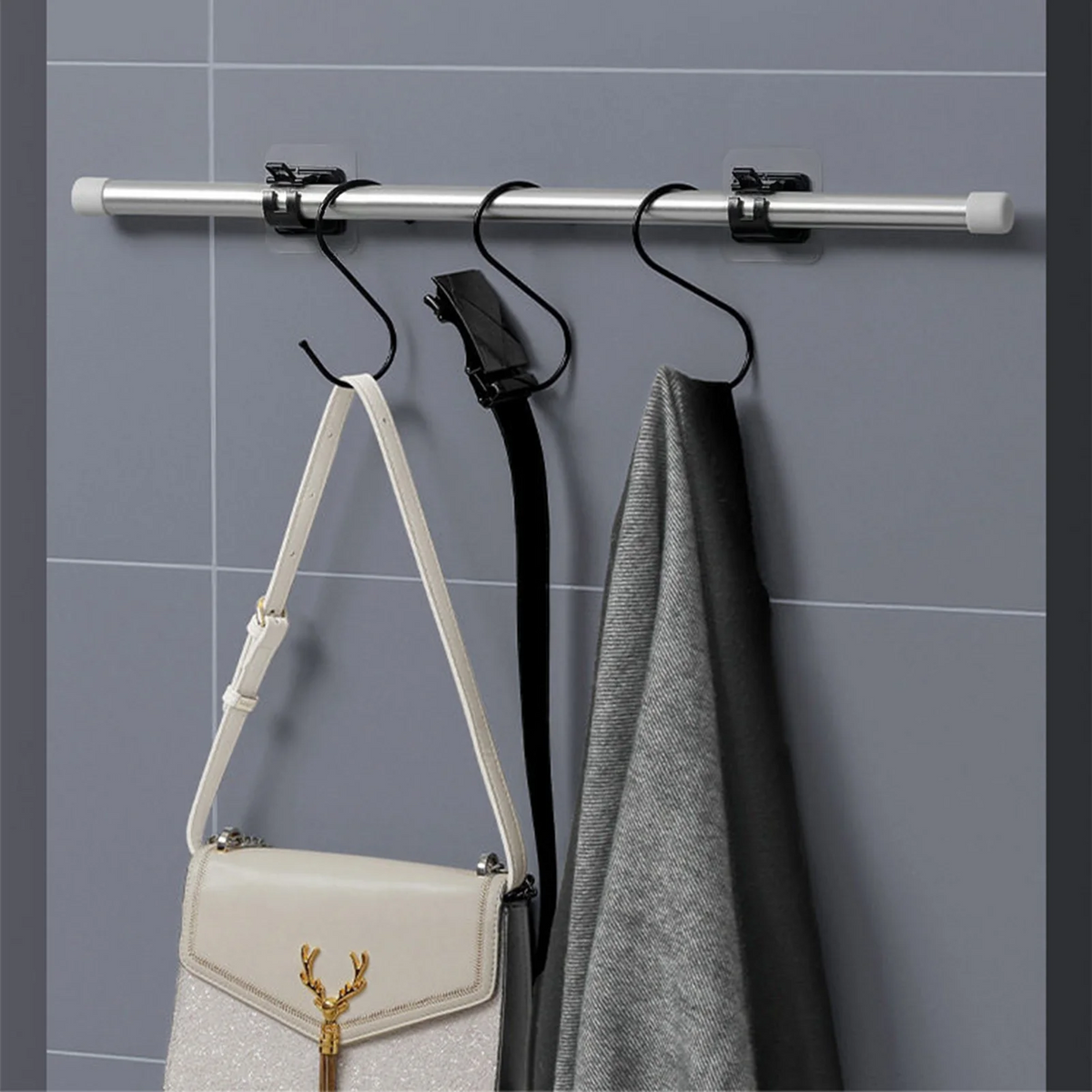 Silver curtain rod clips mounted on a gray tiled wall, with a black garment hanging from one clip.
