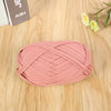 A ball of pink flat thread yarn lying on a wooden surface next to some paper and a small yellow flower.