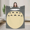 A person is holding up a fleece throw blanket featuring the Totoro character face design.