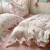 A floral bedding set featuring white fabric with pink and green floral patterns is displayed on a bed.