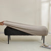 A beige elastic jacquard bench cover is draped over a dark upholstered bench in a bright room.