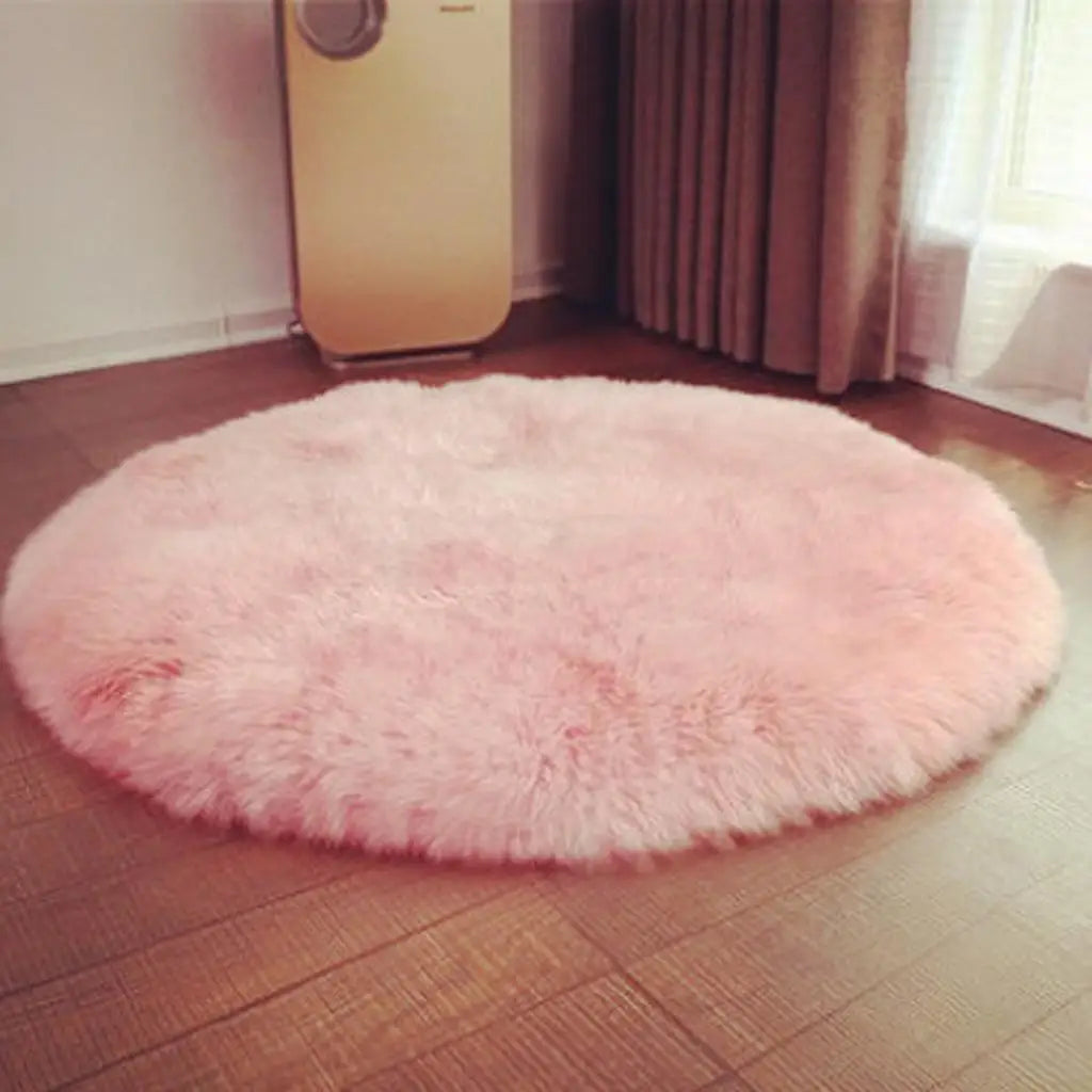 A round, fluffy pink faux fur sheepskin area rug placed on a wooden floor.