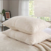 A set of cream embroidered cotton quilted pillow covers resting on a white bed with sheer curtains in the background.