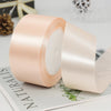Roll of pale pink satin ribbon with decorative trim lying on a white surface.