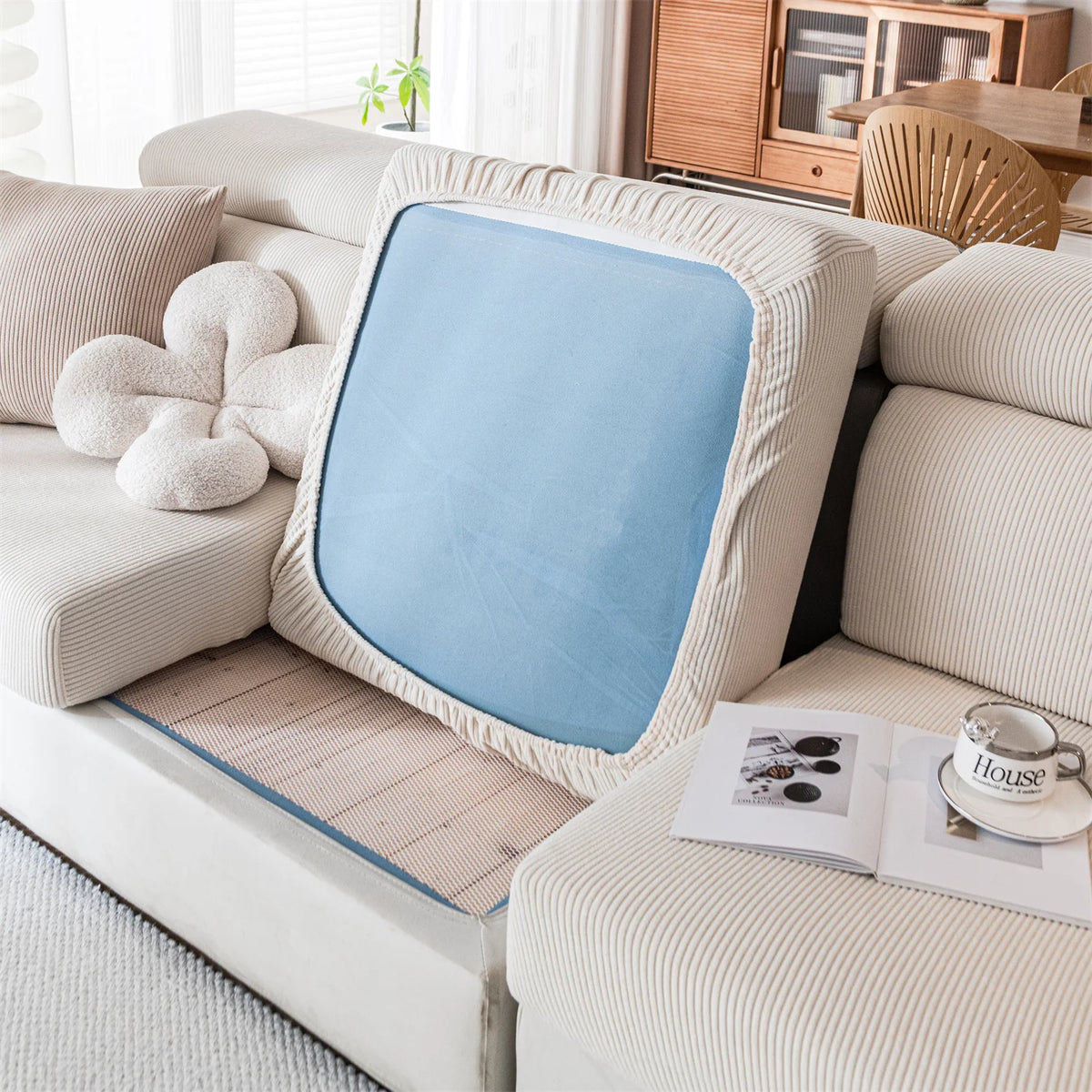 A light beige sofa features a removable blue seat cushion cover with a textured fabric and a white decorative pillow.