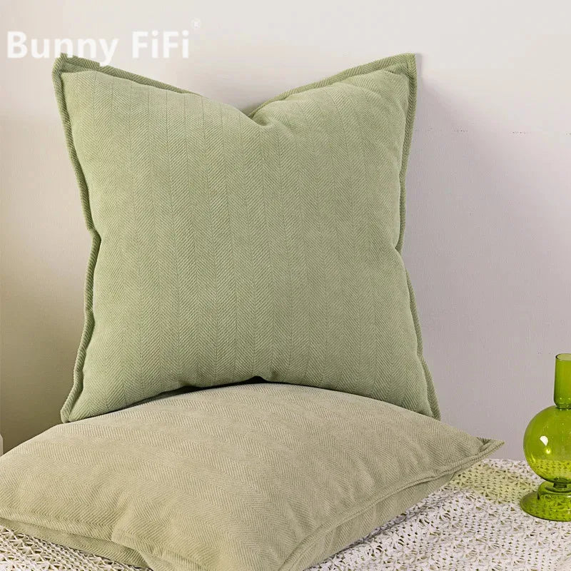A solid sage green chenille throw pillow resting on a white lace surface.