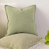 A solid sage green chenille throw pillow cover resting on a white lace surface.