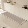 A long, rectangular gray non-slip kitchen floor mat is placed on a light tiled floor in front of a white cabinet with an inte