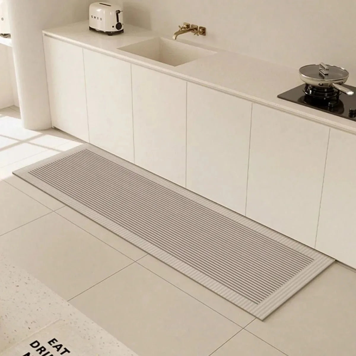 A long, rectangular gray non-slip kitchen floor mat is placed on a light tiled floor in front of a white cabinet with an inte