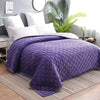 Purple plush velvet quilted bed cover blanket spread on a bed with a light gray background.