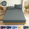 A gray fitted bed sheet set displayed on a wooden bed frame with pillows and a decorative mirror in the background.