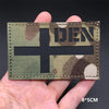 A rectangular tactical patch featuring a dark cross on a camouflage background held in a hand.