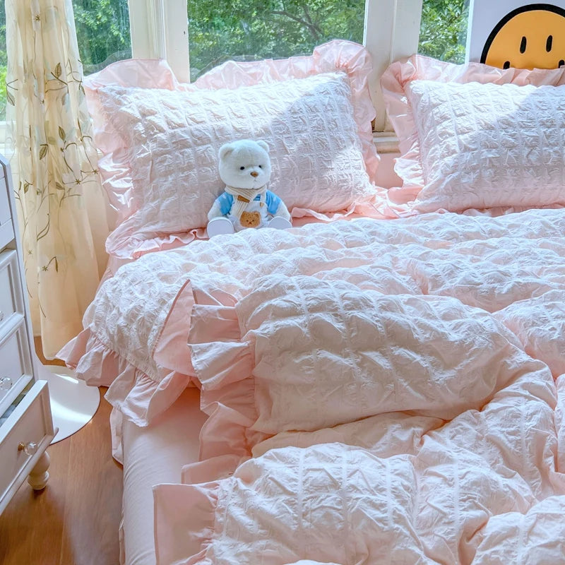 A pink lace seersucker duvet cover set with ruffled fabric and a white teddy bear on a bed.