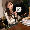 A young woman holds a black 8 ball plush pillow with a white number on it in a studio setting.