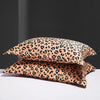 A set of two leopard print silk satin pillowcases in a tan and black pattern resting on a white surface.