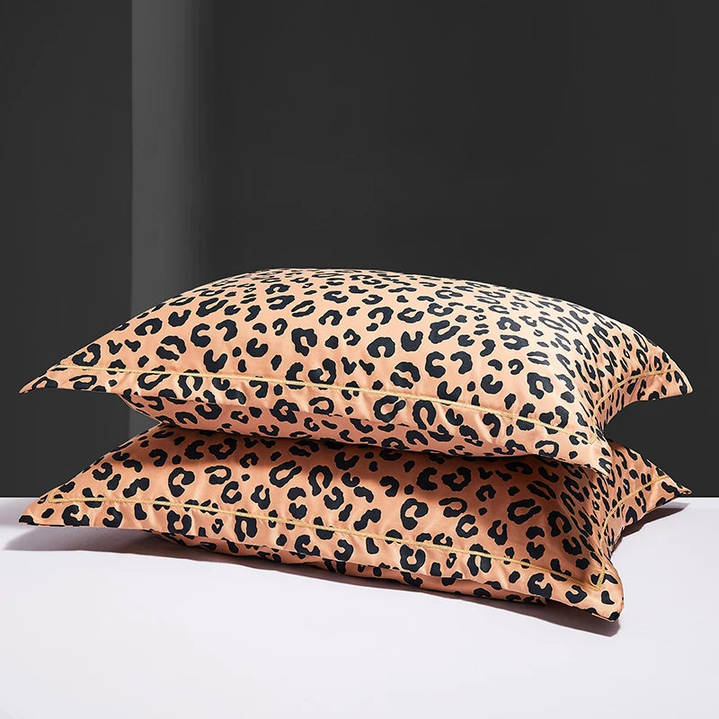 A set of two leopard print silk satin pillowcases in a tan and black pattern resting on a white surface.