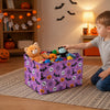 A purple storage basket filled with Halloween-themed items like skulls and bats sits on a rug next to a child.