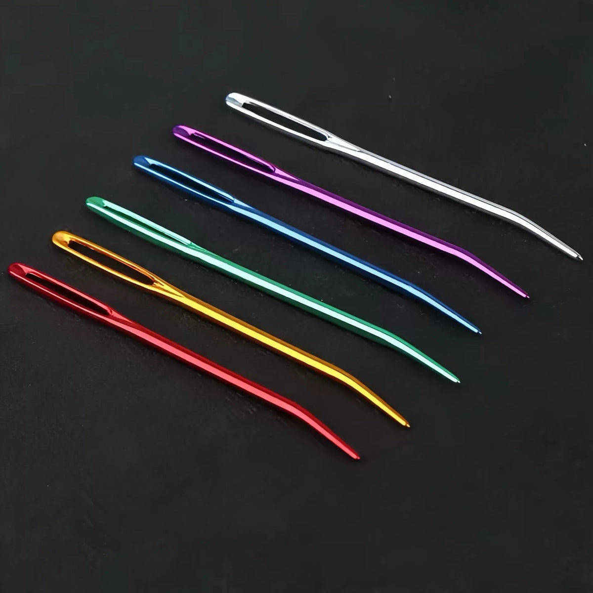 A collection of twenty aluminum knitting needles and sewing pins in various colors laid out on a dark surface.