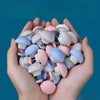 A hand holds a pile of small, round silicone quilt clips in various pastel colors like pink, blue, and white.