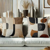 A close-up of a decorative pillow cover featuring geometric shapes in beige, black, and terracotta tones.