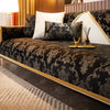 A luxurious dark velvet sofa cover featuring intricate gold embroidery and a light cream accent pillow.