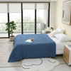 A deep blue pure cotton gauze throw blanket is draped over a bed in a bright, modern bedroom.