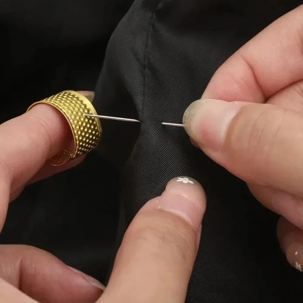 A hand is using a gold-colored sewing needle to mark fabric on a black garment.
