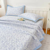 A light blue floral quilted bedspread with a pale blue trim is displayed on a white bed.