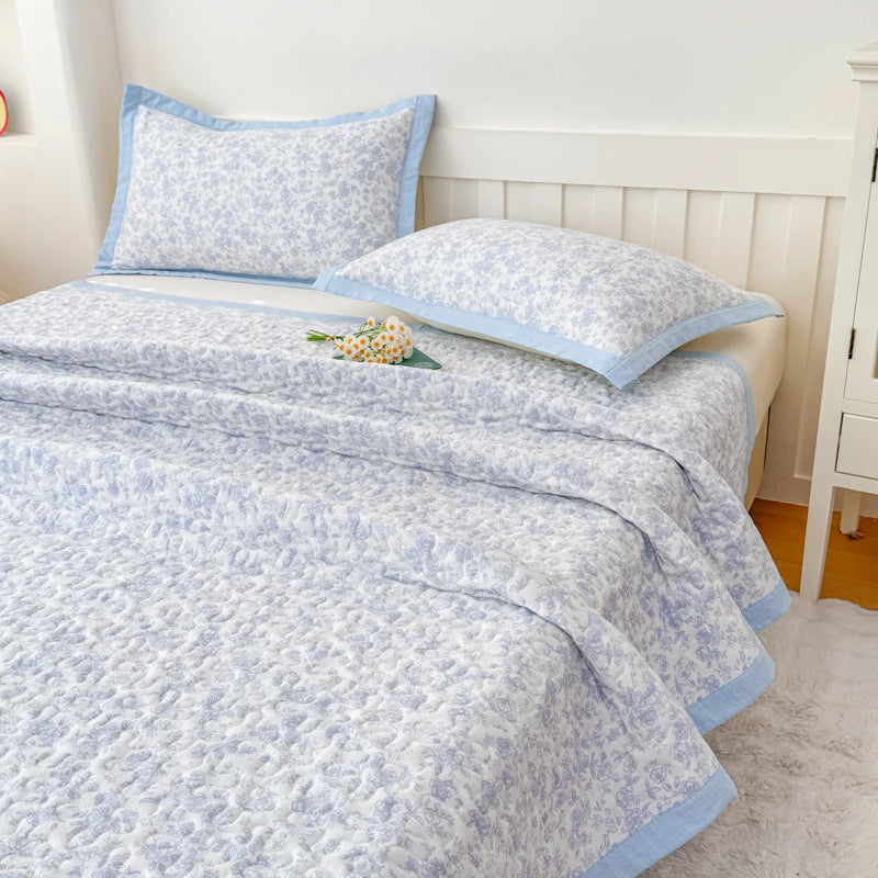 A light blue floral quilted bedspread with a pale blue trim is displayed on a white bed.