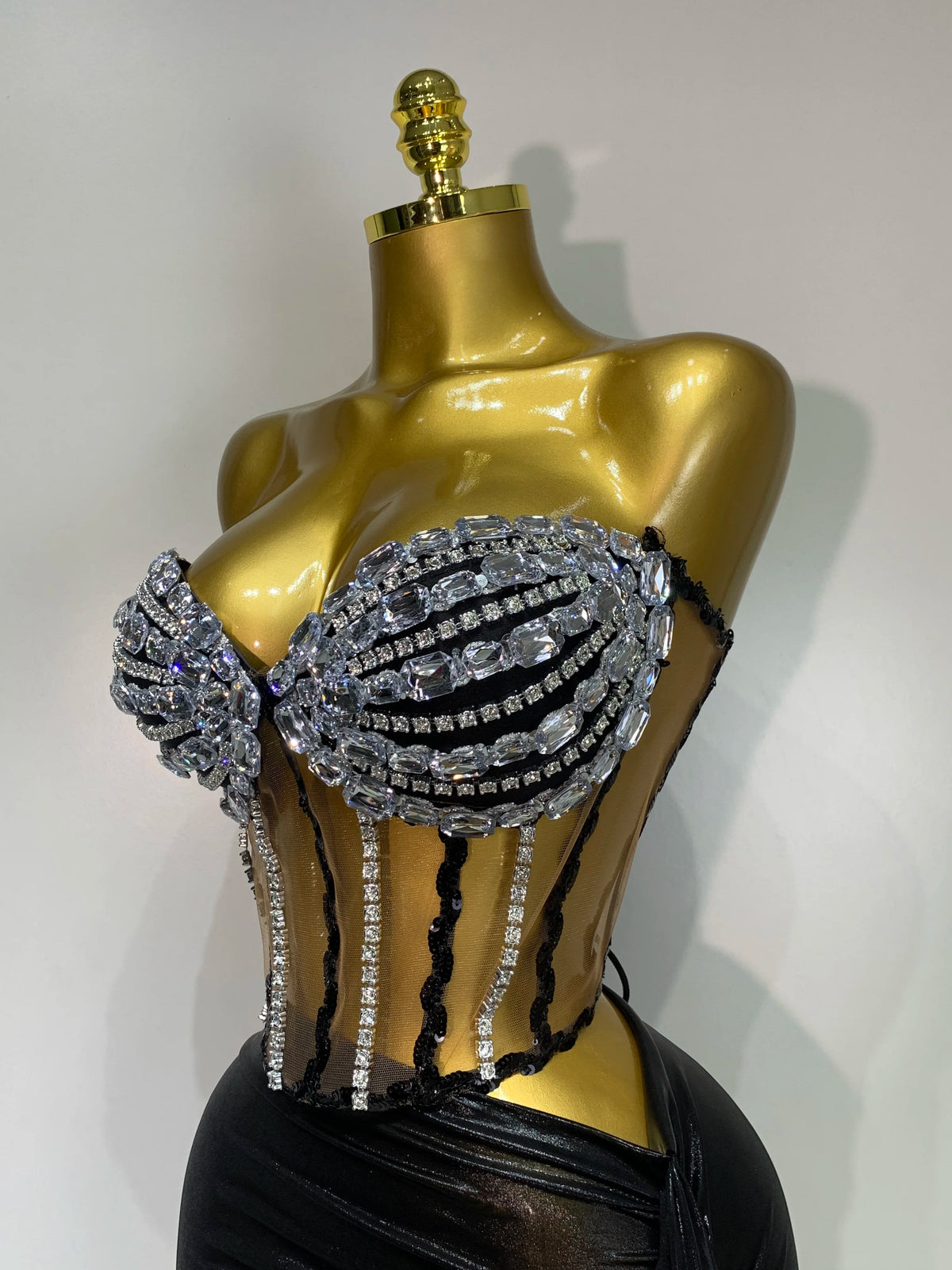 A gold mannequin displays a sparkly diamond two-piece performance set featuring black mesh and rhinestones.