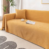A mustard yellow waterproof sofa cover blanket draped over a sofa on a light rug.